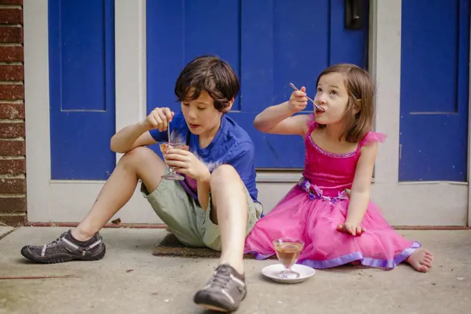Two little children sit on a stoop eating  chocolate ice cream