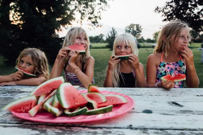 siblings sitting at picnic table outside eating watermelon in summer