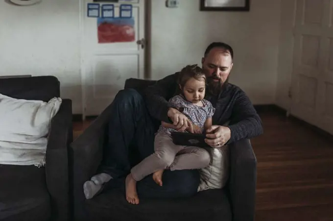 Dad and young daughter playing on tablet during isolation