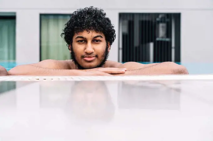 Young Arabian man with curly hair leaning on the edge of a pool