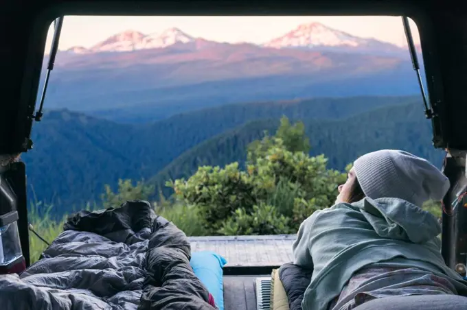 Young woman laying in back of truck looking out at mountains