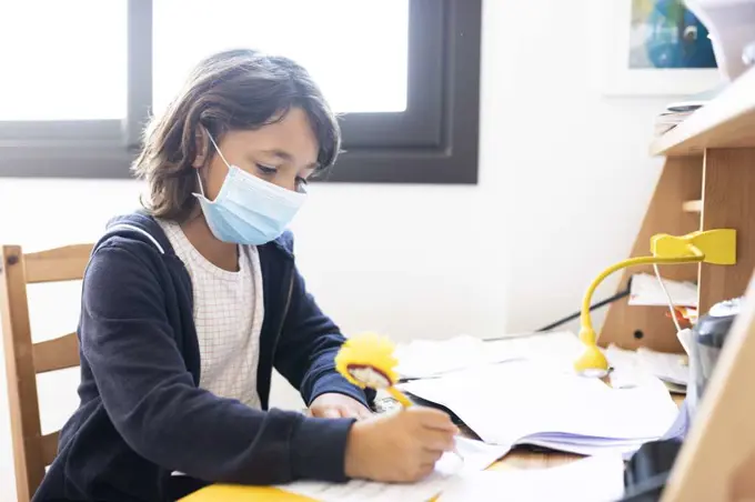 Young spanish boy doing homework while using a mask