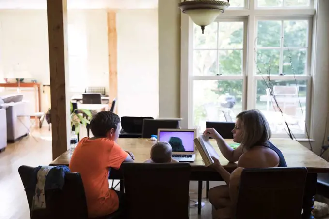 Mom and Toddler Son Watching Laptop Sit With Teenage Cousin at Table