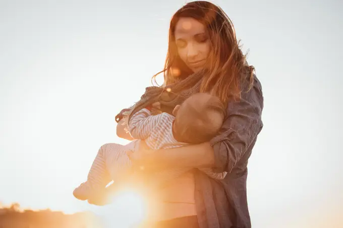 Mom smiling breastfeeding baby outdoors during sunset