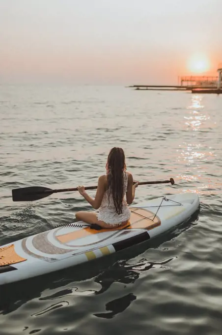 young surfer girl sitting on a Board with a paddle sunset