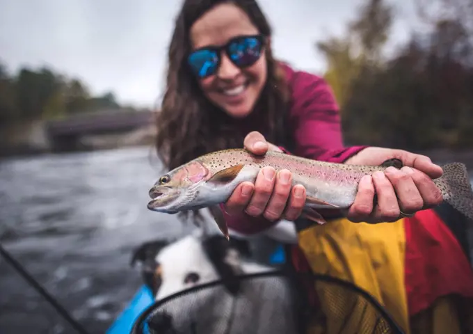 Woman smiling while holding a rainbow trout in boat