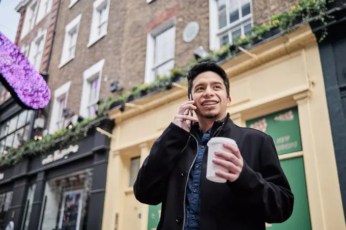 latino young man talking on the phone holding a cup of coffee on the street