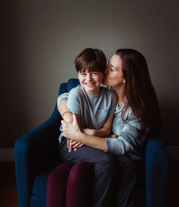 Woman hugging and kissing her son as he sits in her lap on a chair.