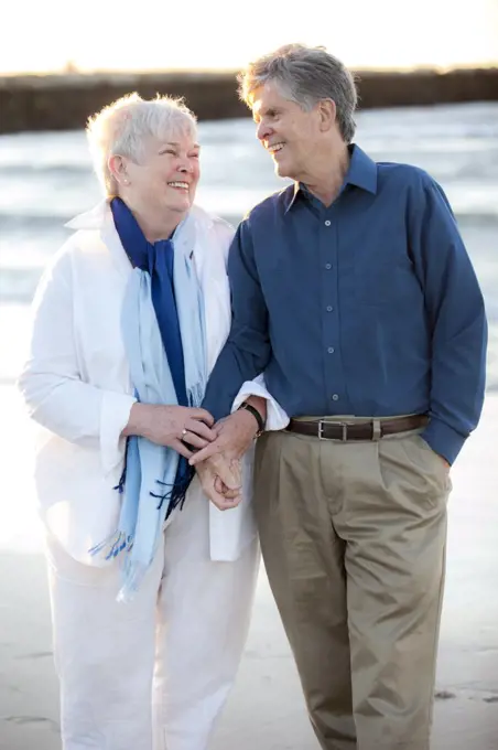 Portrait of older married couple holding hands and laughing at Beach