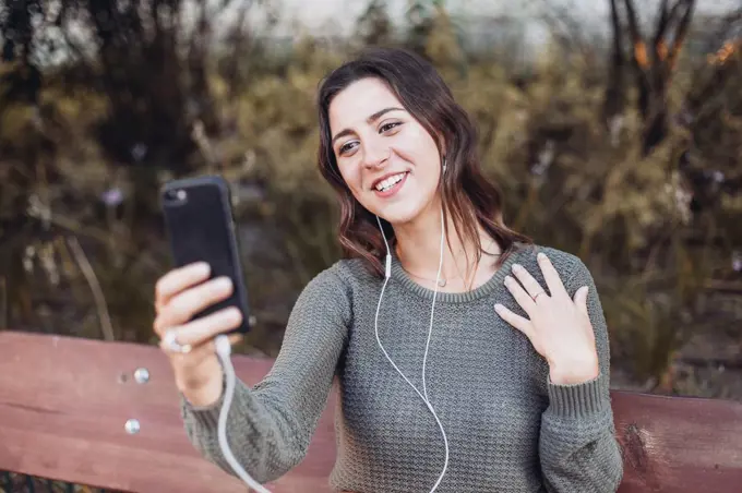 Young woman having a video call, on a bench outdoors