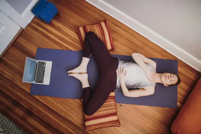 Woman in athletic wear with laptop computer relaxes on floor of home