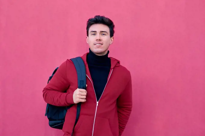 Handsome student man poses with a backpack on a pink background