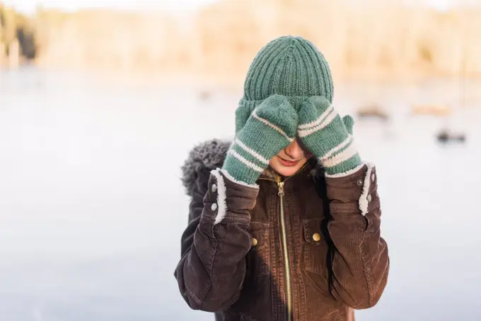 winter portrait of boy with wooly hat hiding behind his mittens