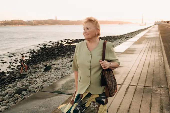 Elder woman standing alone at the riverside in Lisbon, looking f