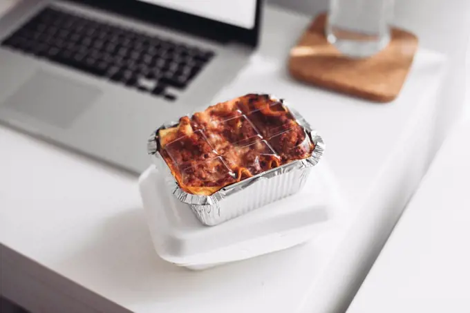 A takeaway box with lasagna, a laptop. Concept of eating at home