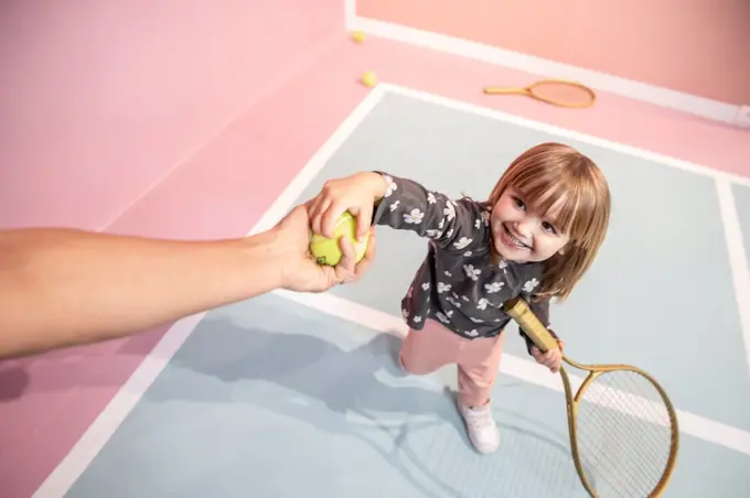 Little girl having fun and playing tennis while someone giving a tenni