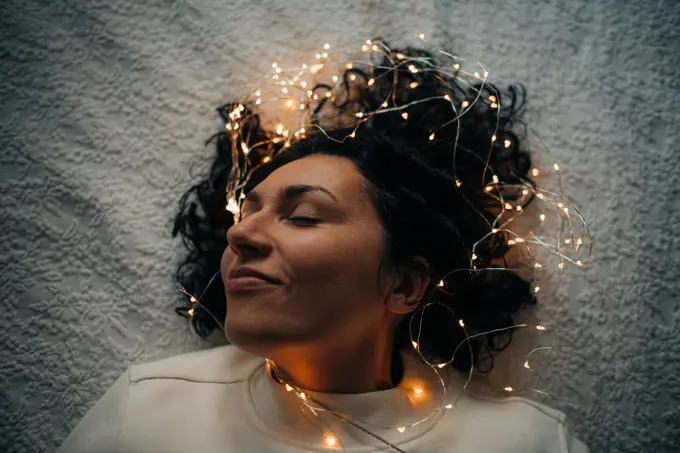 Woman lying down with tangled string lights in her hair, smiling