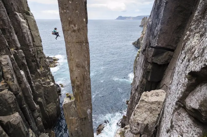 Female rockclimber falls as she tries to climb The Totem Pole, an exposed sea stack which rises out of the ocean in Cape Hauy, Tasman National Park, Tasmania, Australia.