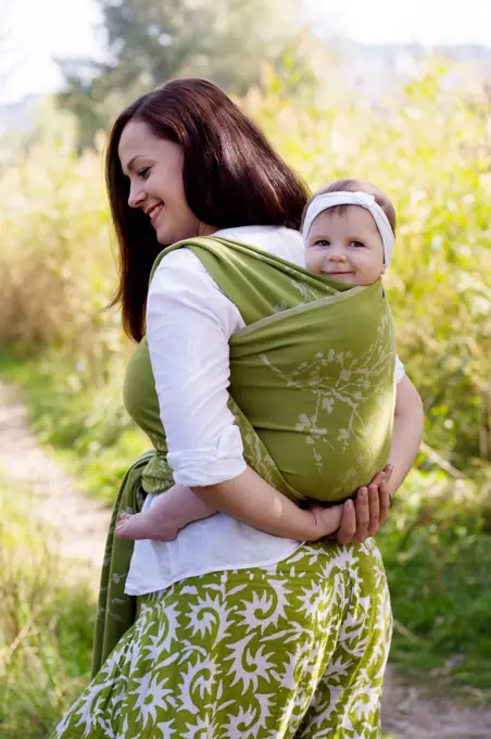 Happy smiling family with mom and girl back in green sling carrier