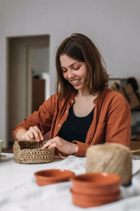 Young woman knits from jute and smiles