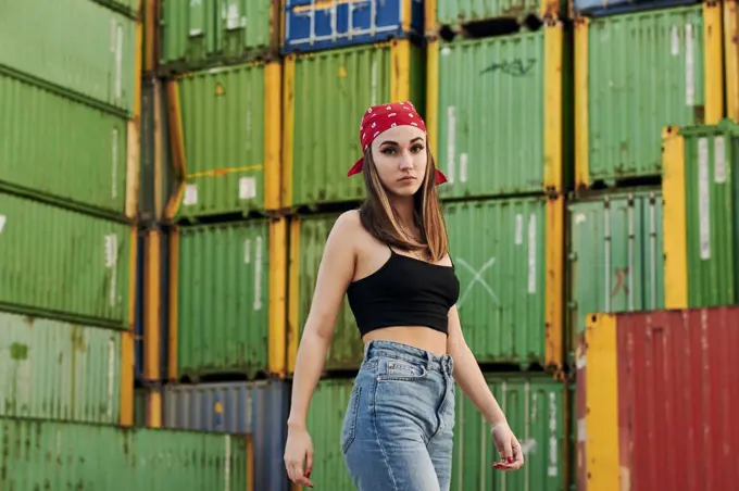 Young woman in urban clothing poses surrounded by shipping containers