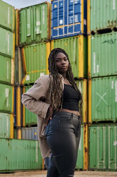 Black woman in urban clothing poses surrounded by shipping containers