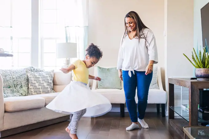 Smiling mother looking at daughter practicing dance in living room at home