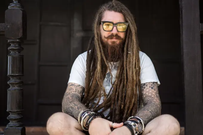 hipster guy with dreadlocks and tattoo sitting on the beach in thailan
