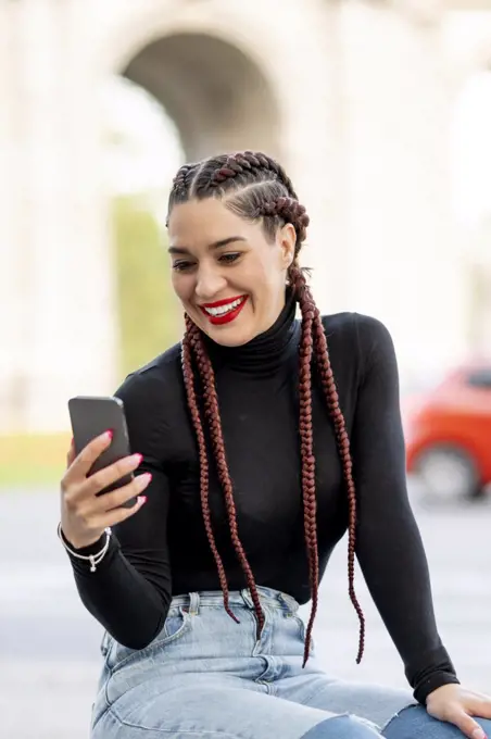 Beautiful woman with braids using a mobile phone and smiling