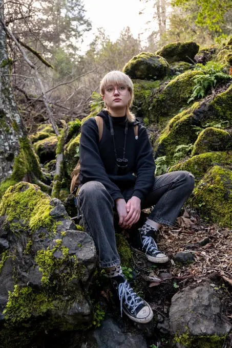 Young hiker sitting on mossy stones taking break looking calm