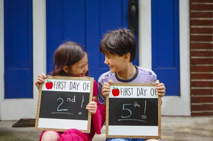 Two happy children sit together on stoop holding Back-to-School signs