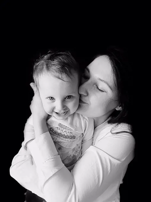 black and white portrait of mother hugging and kissing smiling girl
