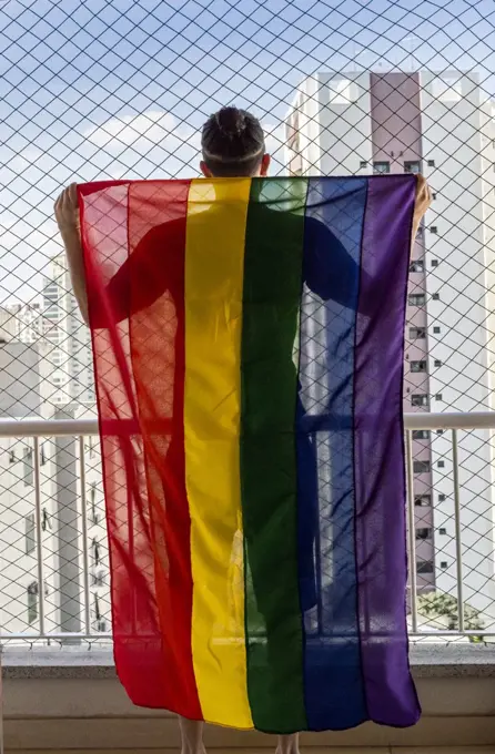 Gay man holding the rainbow flag symbol of gay pride on a balcon