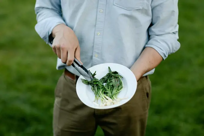 Man's hands holding a platter of grilled and wilted ramps