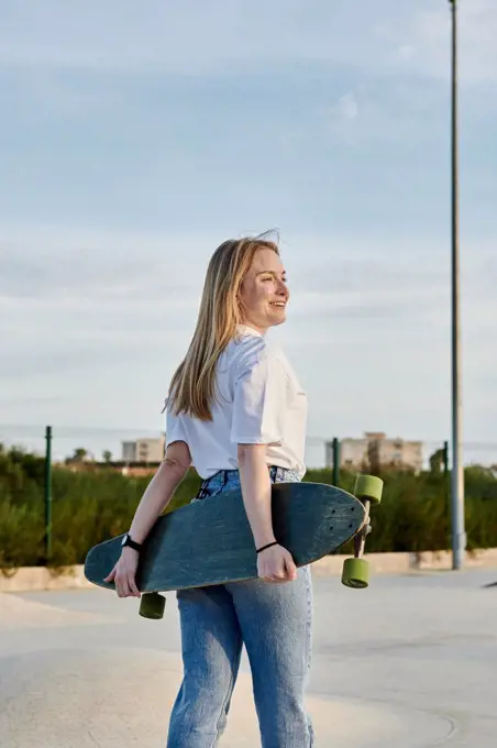 Young blonde woman smiling and having fun holding a skateboard