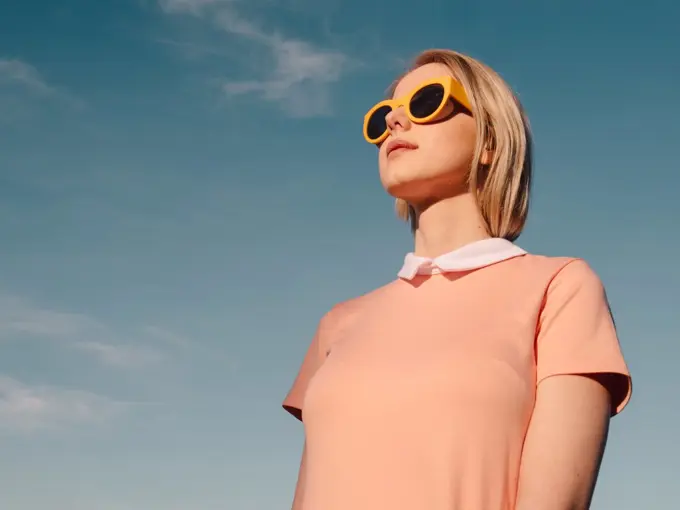 Style woman in pink dress with yellow glasses on blue sky backgr