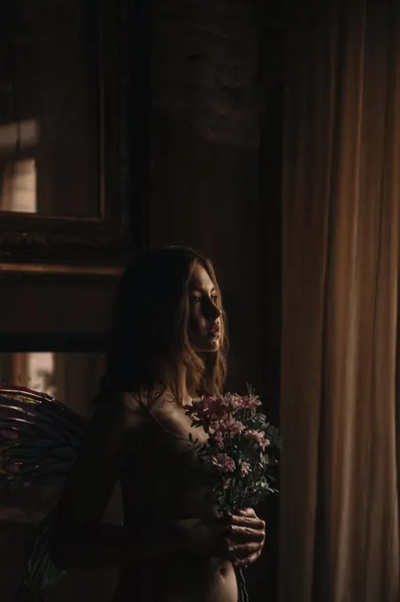 A girl with wings. standing with flowers in her hands in the room.