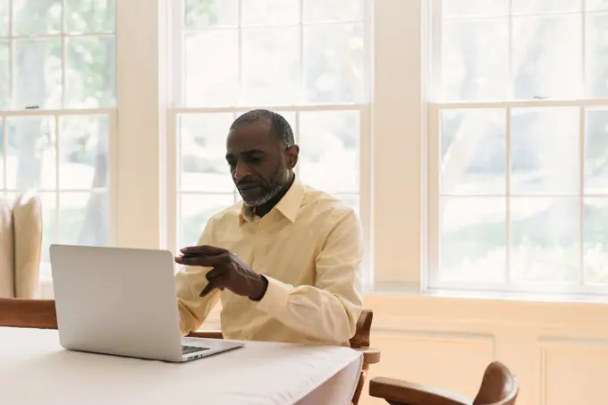 Man gesturing to his laptop while working from bright home table