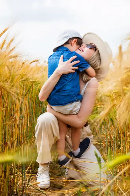 happy mom with son hugging on wheat field 