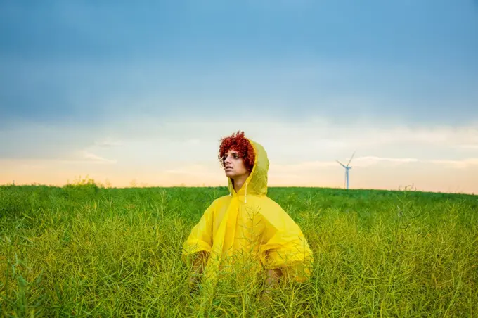 Young redhead guy in yellow raincoat on green rapeseed field 