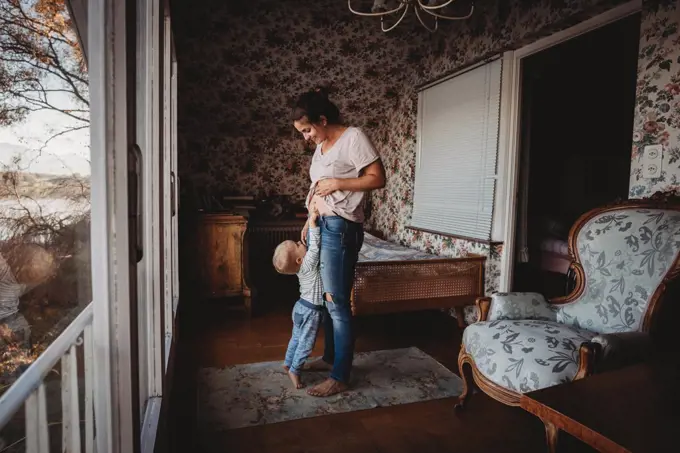 Toddler touching mom's belly in vintage room with wallpaper