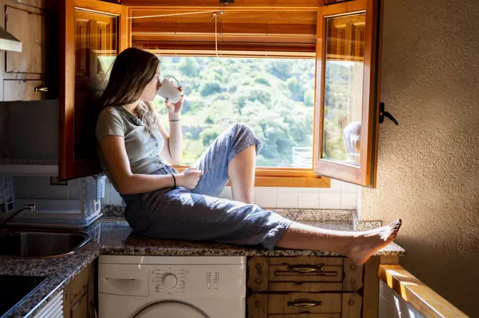 Teenage woman sitting looking out the window drinking coffee