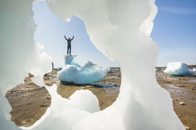 Man standing on top of iceberg, arms raised, Baffin Island.