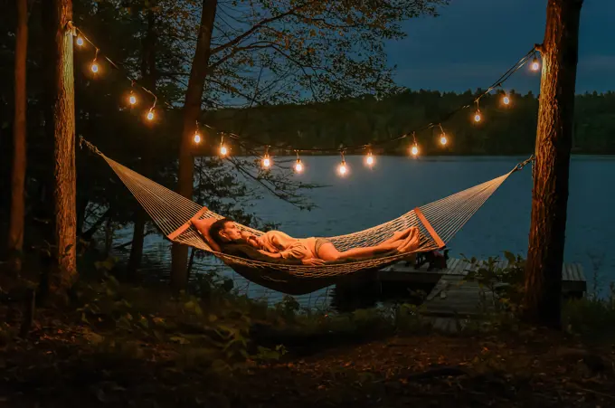 Couple laying in a hammock together on a summer evening by the lake.