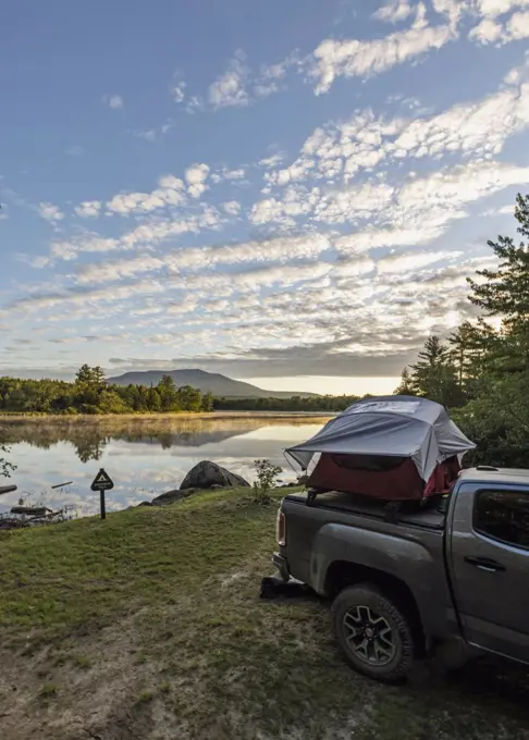 Truck with tent sits next to peaceful river with mountain, Maine