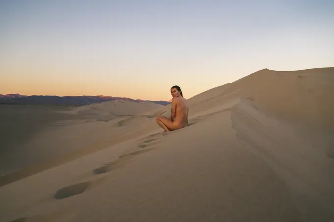 Naked female sitting on a sand dune at sunset