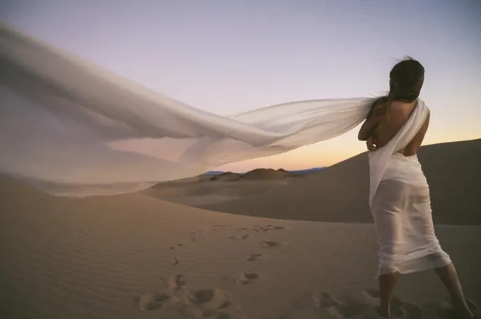 Naked female posing on a sand dune wrapped in a white cloth
