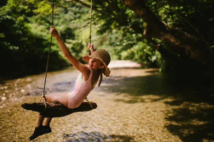 Young girl on tree swing over a river in summer