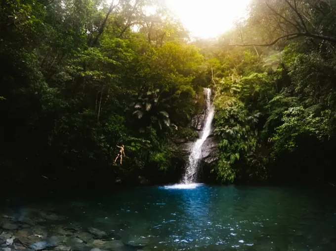 Boy enjoying tropical pool with gorgeous waterfall in green landscapes