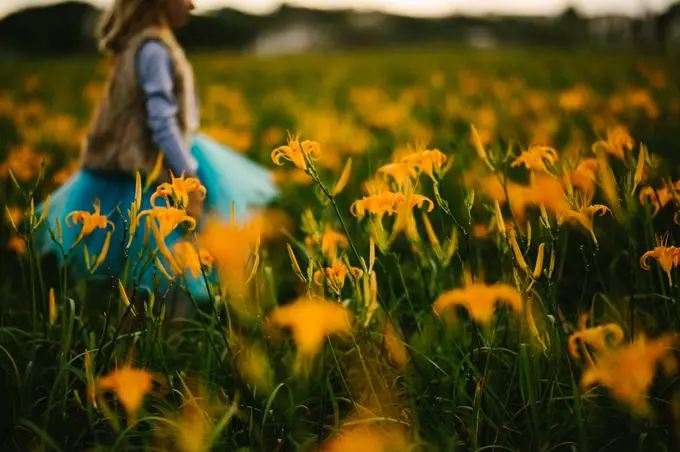 Girl walking through fall orange lily flower field